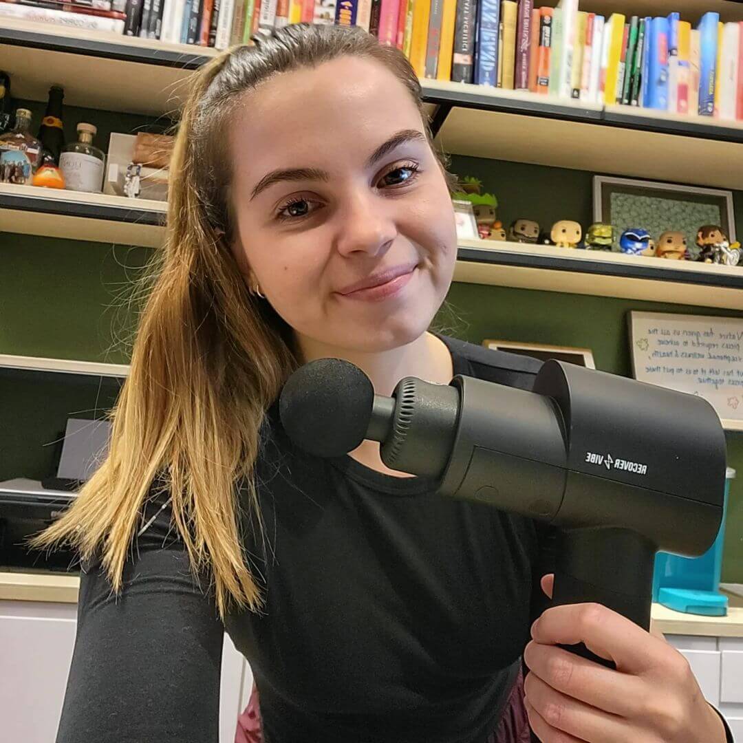 woman holding Recover Vibe Blast massage gun in her hand and smiling
