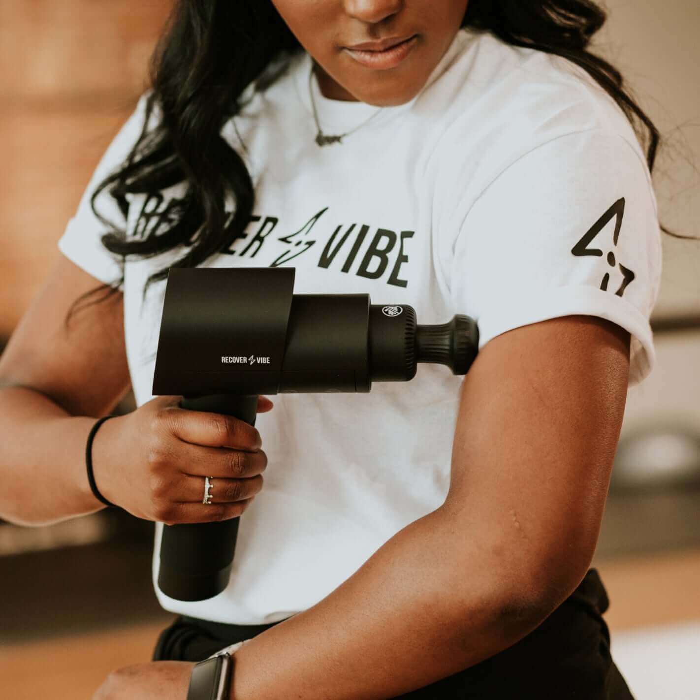 Woman using Recover Vibe Blast massage gun on her arm